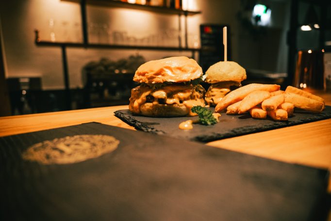 Zwei Burger mit Pommes auf einem schwarzen Servierbrett in einem Restaurant.