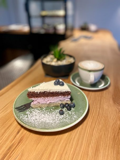 Kuchen mit Beeren und Sahne, serviert auf einem grünen Teller mit einer Tasse Kaffee.
