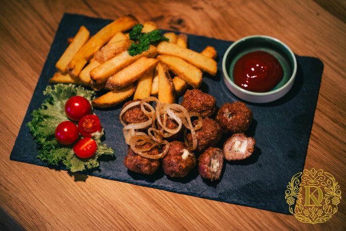 Frittierte Kartoffelstäbchen, Frikadellen, frischer Salat und Ketchup auf einem schwarzen Teller.